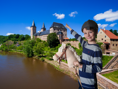 Ein Junge mit einem Stockpferd zeigt auf Schloss Rochlitz 